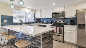 A modern kitchen with white cabinets, a large island with stools, a microwave, oven, and a refrigerator. - Heated Pool, Quiet Neighborhood (Phoenix)