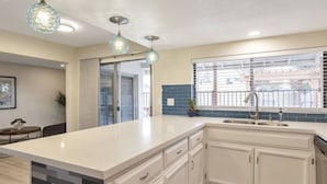 A modern kitchen with a large island, white cabinetry, a window with blinds, and pendant lighting. - Heated Pool, Quiet Neighborhood (Phoenix)