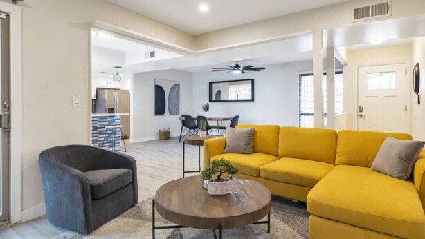 A spacious living room with a yellow sofa, a dark armchair, and a round coffee table. - Heated Pool, Quiet Neighborhood (Phoenix)