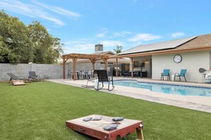 Un patio trasero con piscina, una terraza techada y una estructura de juego de madera.