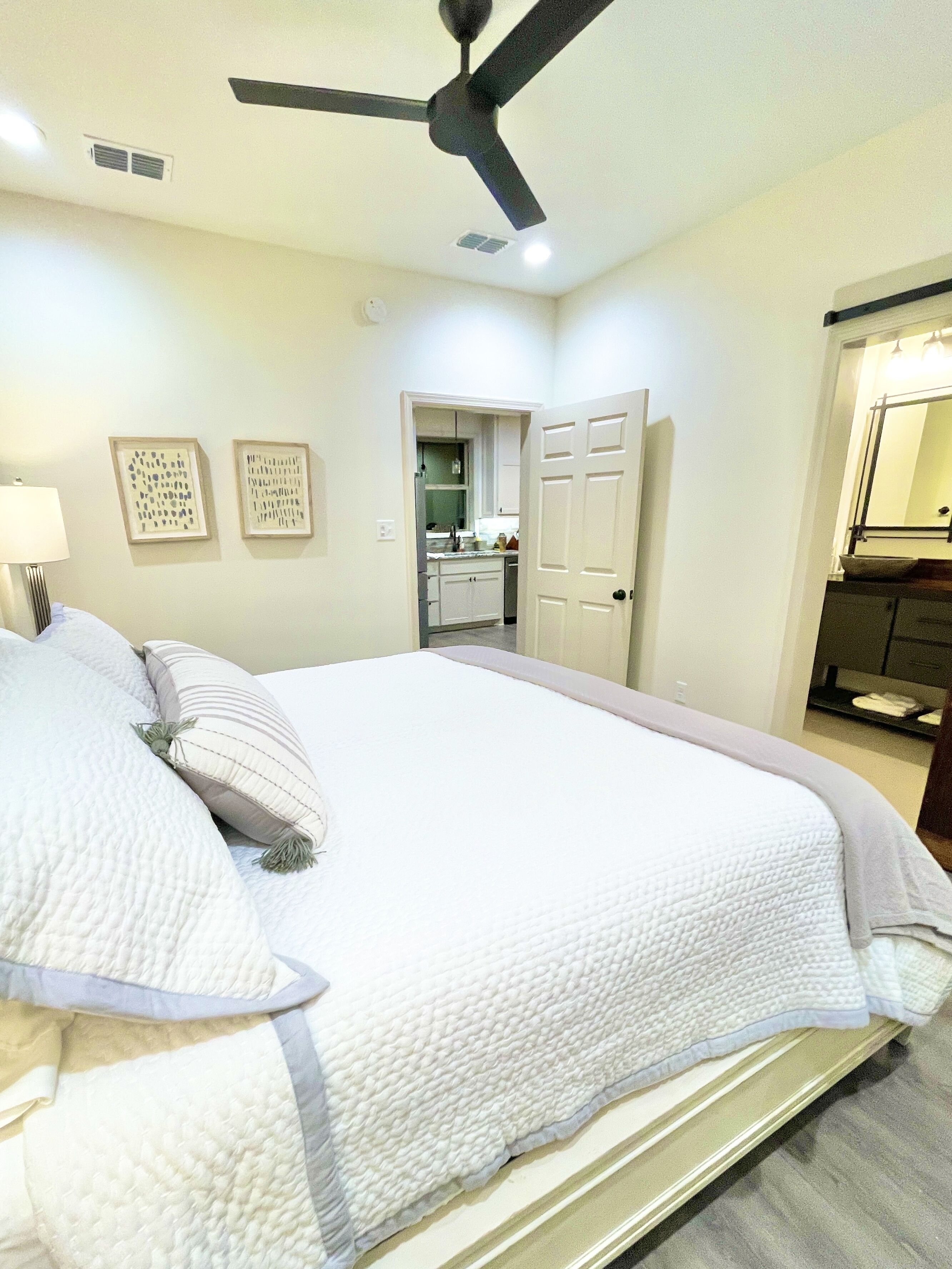 A bedroom with a bed, a ceiling fan, and a view into the kitchen.