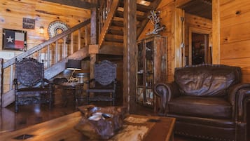 A rustic wooden interior with a leather sofa, ornate chairs, a wooden table, and a staircase.