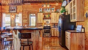 A rustic wooden kitchen with a central island, bar stools, and a 'HOME' sign above the cabinets.