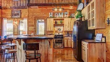 A rustic wooden kitchen with a central island, bar stools, and a 'HOME' sign above the cabinets.