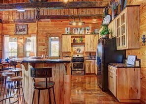 A rustic wooden kitchen with a central island, bar stools, and a 'HOME' sign above the cabinets.
