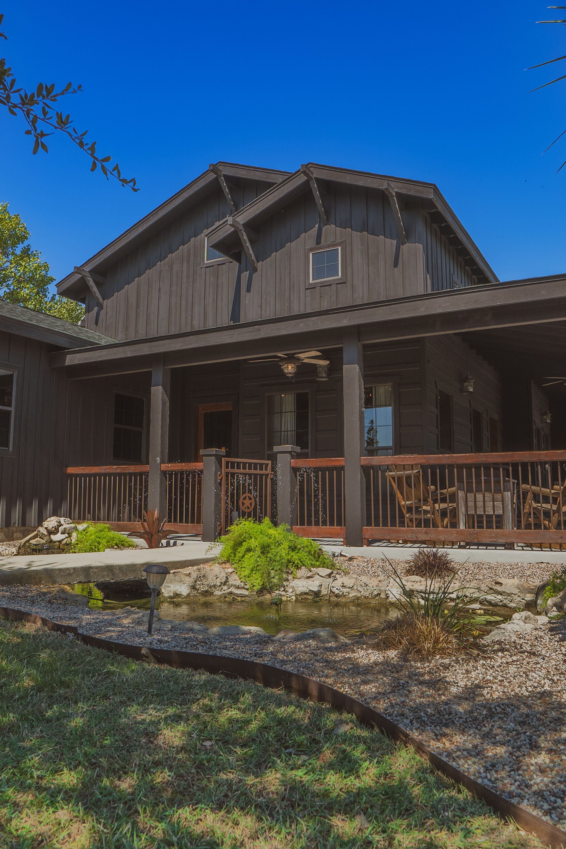 A two-story wooden house with a porch, a small pond, and a stone pathway.