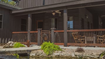 A two-story wooden house with a porch, a small pond, and a stone pathway.