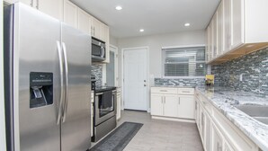 A modern kitchen with stainless steel appliances, white cabinetry, a built-in oven, and a tiled backsplash.