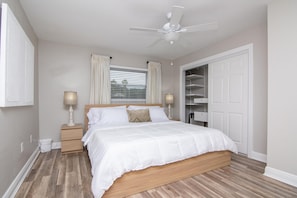 A bedroom with a wooden bed, white curtains, a ceiling fan, and a white wardrobe.