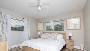 A bedroom with a bed, bedside tables, a ceiling fan, and two windows with blinds.