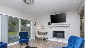 A modern living room with a fireplace, a flat-screen TV mounted above it, and a dining area with a table and chairs.