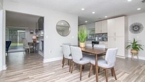 A modern kitchen with white cabinets, a dining area with a wooden table and grey chairs, and a large mirror on the wall.