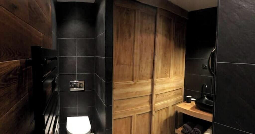 Une salle de bain avec un meuble-lavabo en bois, un lavabo noir et des toilettes.