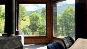 A room with a large window offering a view of a mountainous landscape. A wood-burning stove is visible in the corner.