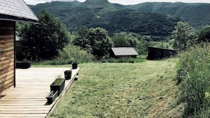 A wooden cabin with a deck overlooking a grassy landscape and distant mountains.