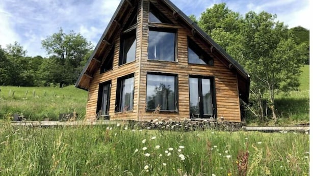 A wooden cabin with a gabled roof, multiple windows, and a stone foundation.