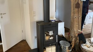 A wood-burning stove with a chimney, a door, and a basket of firewood. - Loft apartment in the BENEFIZIUM Anno 1713 (Denklingen)