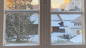 A window with a view of a building with a tower, trees, and a snowy landscape. - Loft apartment in the BENEFIZIUM Anno 1713 (Denklingen)