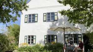 A white building with green shutters and a patio area with an umbrella. - Loft apartment in the BENEFIZIUM Anno 1713 (Denklingen)