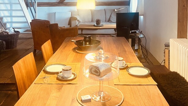 A dining area with a wooden table set for four, a hanging light fixture, and a view of a loft space with exposed wooden beams. - Loft apartment in the BENEFIZIUM Anno 1713 (Denklingen)