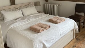 A bedroom with a wooden ceiling, a bed with white linens, a bedside table with a lamp, and a radiator. - Loft apartment in the BENEFIZIUM Anno 1713 (Denklingen)