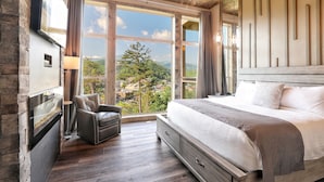 Un dormitorio con una cama grande, chimenea, sillón de cuero y vistas al exterior.