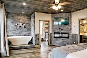 A modern bathroom with a freestanding bathtub, a stone wall, and a mounted TV.