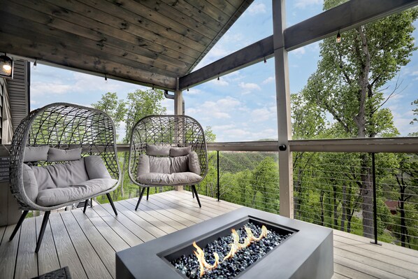 Una terraza de madera con dos sillas grises acolchadas y una chimenea integrada.