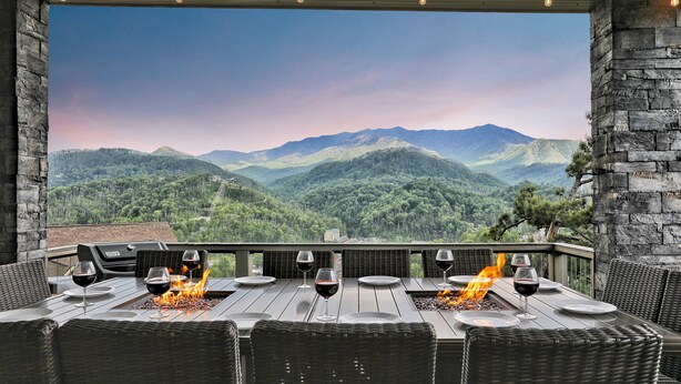 Un área de comedor al aire libre con vista a montañas, una fogata y paredes de piedra.