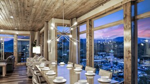 Un comedor con una mesa grande dispuesta para una comida, ventanas amplias con vista a la ciudad y techo de madera.