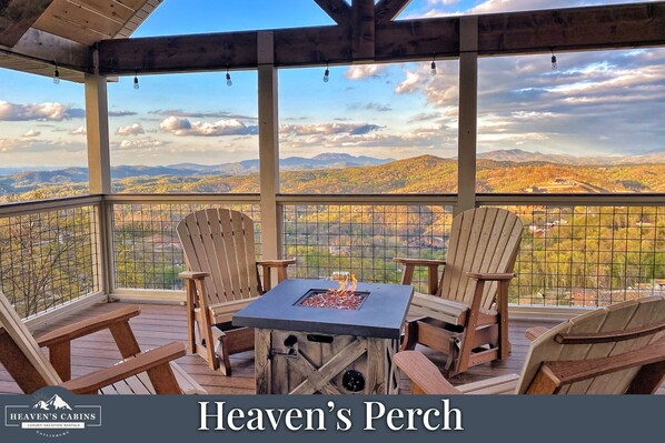 A covered outdoor seating area with Adirondack chairs and a square table with a fire feature, overlooking a scenic landscape.