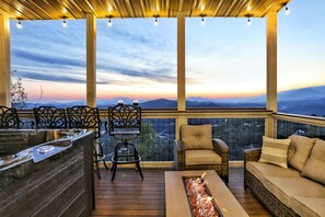 A covered outdoor area with a wooden deck, a built-in grill, wicker furniture, and a view of distant mountains.