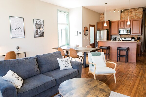 Un salon moderne comprenant un canapé, des fauteuils, une table basse et un coin repas avec une table et des chaises. Il y a également une cuisine équipée de meubles en bois et d’un réfrigérateur.