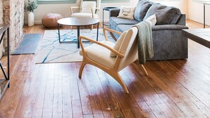 Un salon spacieux doté d’un plancher en bois, d’un canapé gris, d’une chaise en bois et d’un ventilateur de plafond.