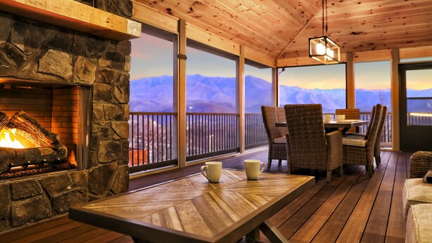 A wooden deck with a stone fireplace, wicker chairs, and a table with two white cups. - EXTRAORDINARY Luxury View Cabin! Game Room! Theater! Porch w/ Fireplace! Hot tub (Gatlinburg)