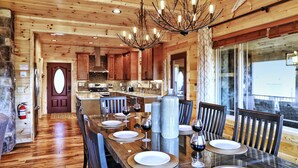 A wooden interior with a dining table set for six, a kitchen in the background, and a stone wall with a fire extinguisher. - EXTRAORDINARY Luxury View Cabin! Game Room! Theater! Porch w/ Fireplace! Hot tub (Gatlinburg)