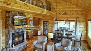 A cozy log cabin interior with a stone fireplace, comfortable seating, and a dining area. - EXTRAORDINARY Luxury View Cabin! Game Room! Theater! Porch w/ Fireplace! Hot tub (Gatlinburg)