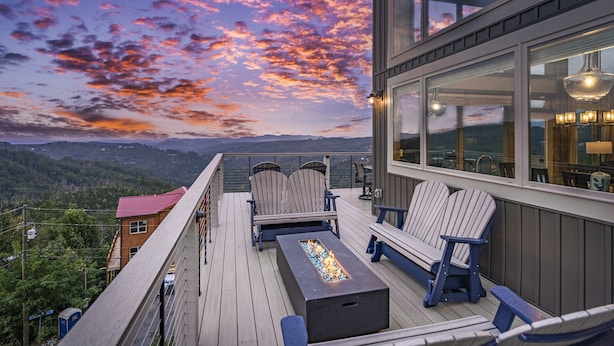 Una terraza con sillas Adirondack y un brasero, con vistas a un paisaje montañoso.