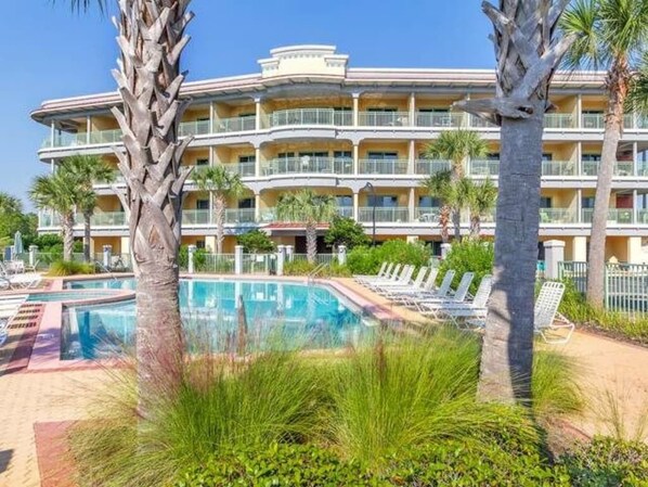A hotel with a pool area, palm trees, and a multi-story building with balconies.