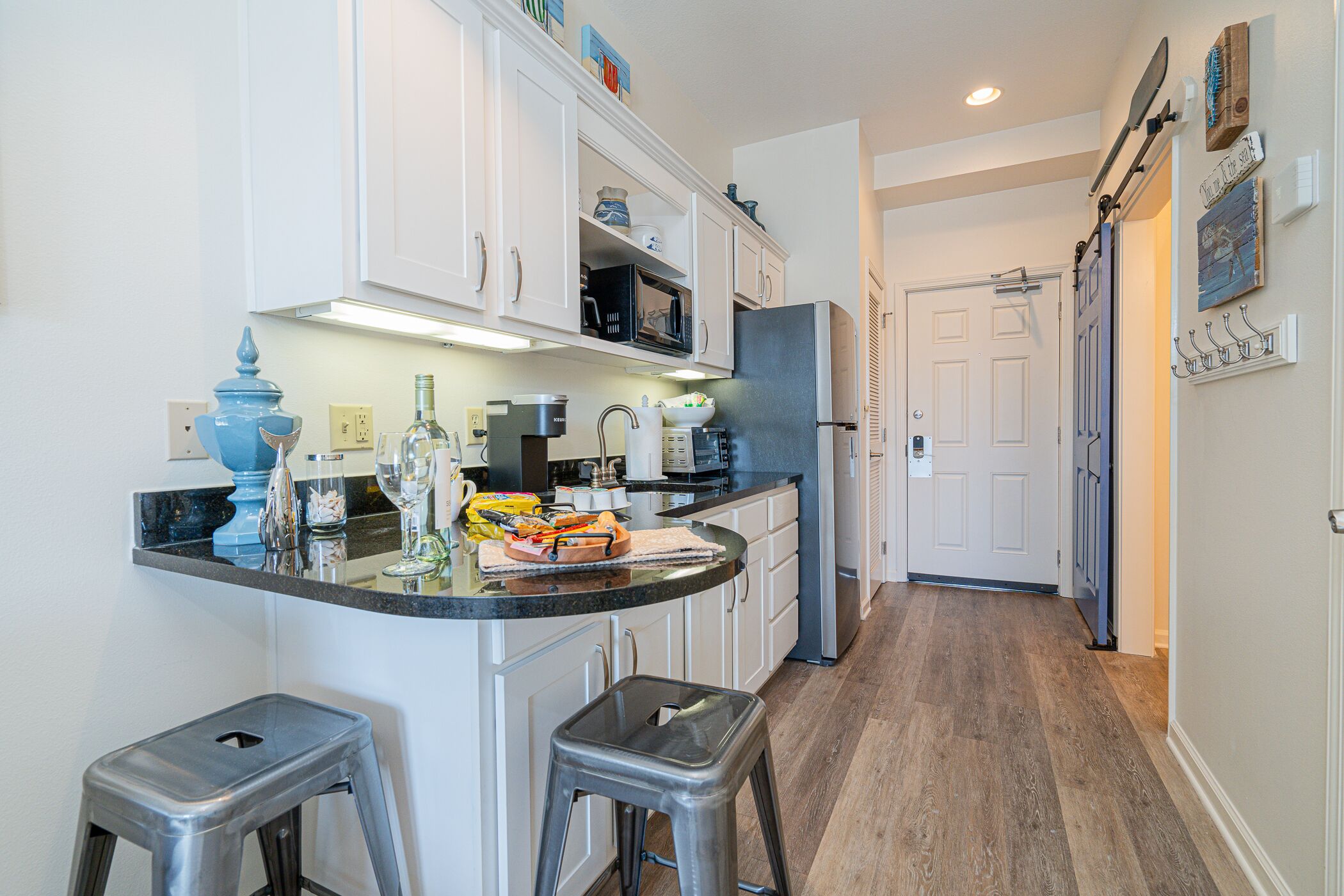 A kitchen with white cabinets, a black countertop, and two stools.