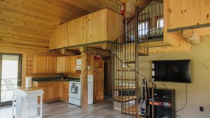 Una cabaña de madera espaciosa con cocina, comedor y una escalera que sube a un nivel superior.
