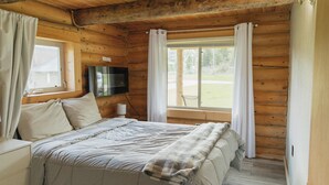 Un dormitorio de cabaña de madera con una cama, un televisor en la pared y una ventana con cortinas.