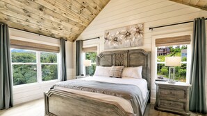 Ein Schlafzimmer mit einem großen Bett, einem Holzkopfende, einem Nachttisch und Blick auf Grünfläche.
