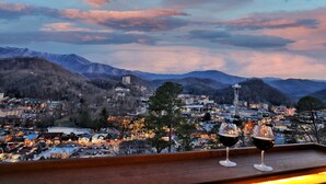 Une vue panoramique d’une ville avec des montagnes en arrière-plan, deux verres à vin sur un plateau et une tour au loin.