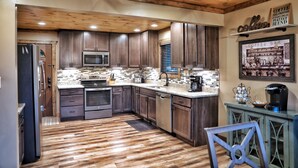 Une cuisine moderne avec des meubles en bois, un réfrigérateur en acier inoxydable, un four à micro-ondes et un coin café.