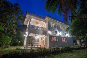 A two-story house with a balcony, multiple windows, and outdoor lighting.