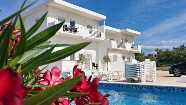 Un bâtiment moderne de couleur blanche, doté d’une piscine et entouré de verdure et de fleurs rouges.