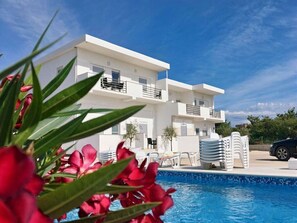 A modern white building with a pool, surrounded by greenery and red flowers. - Apartment Toni - Two Bedroom Apartment with Terrace and Shared Swimming Pool (Nin)