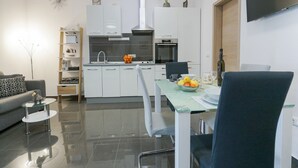 Une cuisine moderne avec des meubles blancs, un four encastré et un coin repas comprenant une table et des chaises en verre.