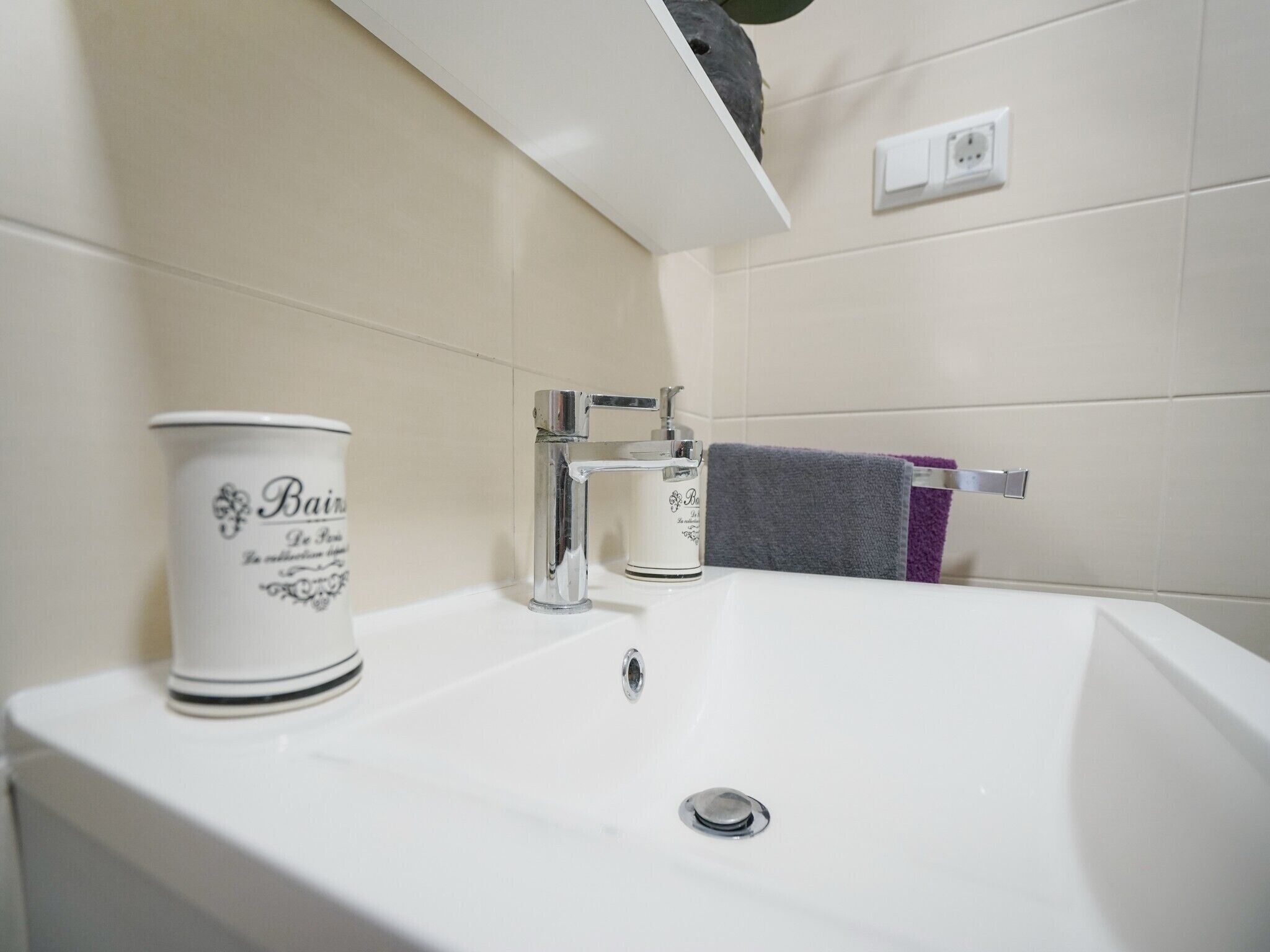 A bathroom with a white sink, a bottle of hand soap, and a towel rack with a purple towel.